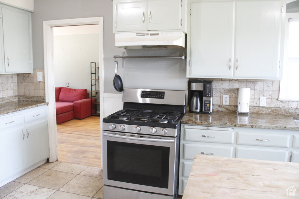 Kitchen with gas range, under cabinet range hood, white cabinets, backsplash, and light stone countertops