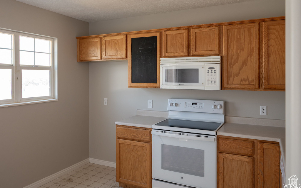 Kitchen featuring white appliances, light countertops, and brown cabinetry
