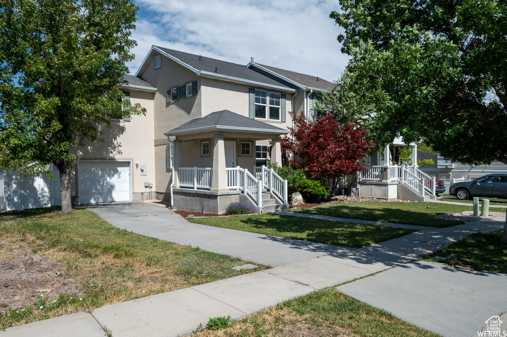 Traditional home featuring driveway, covered porch, stucco siding, an attached garage, and a front lawn