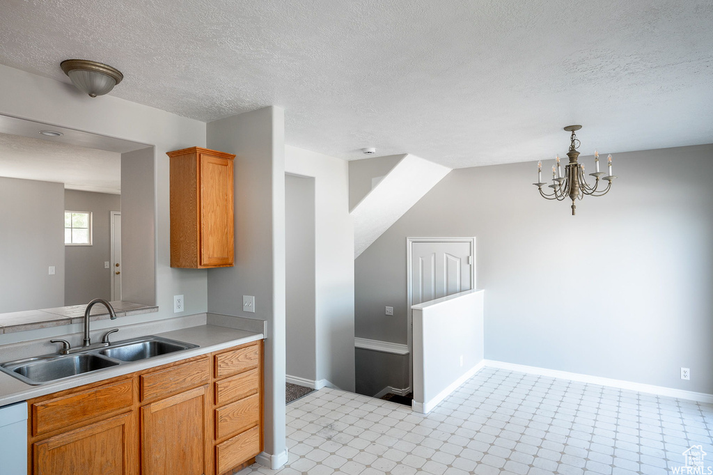 Kitchen featuring light countertops, a textured ceiling, hanging light fixtures, a chandelier, and brown cabinets