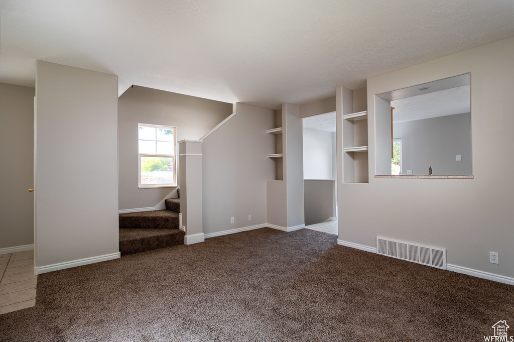 Unfurnished living room featuring carpet and stairs