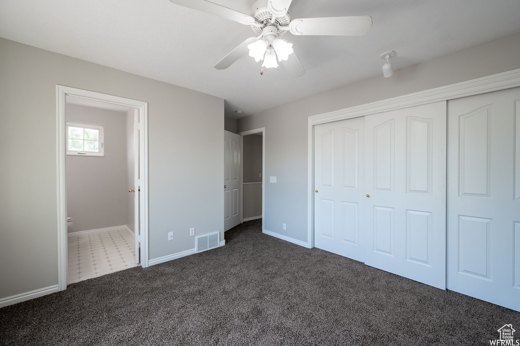 Unfurnished bedroom with dark colored carpet, a closet, a ceiling fan, and ensuite bathroom