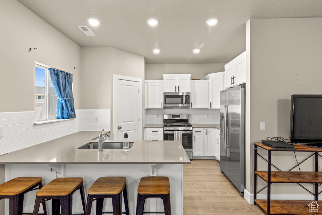 Kitchen with a peninsula, appliances with stainless steel finishes, a kitchen breakfast bar, white cabinets, and light wood finished floors