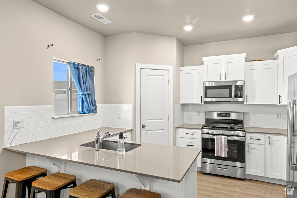 Kitchen featuring stainless steel appliances, a breakfast bar area, white cabinets, a peninsula, and recessed lighting