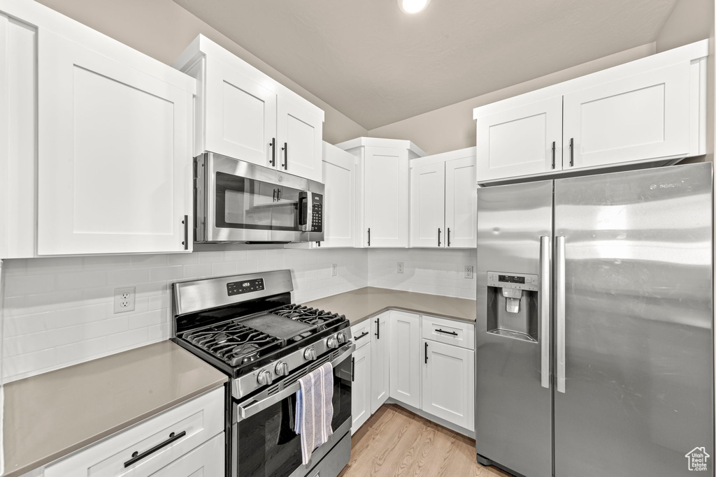 Kitchen with stainless steel appliances, white cabinetry, light wood-style floors, and decorative backsplash