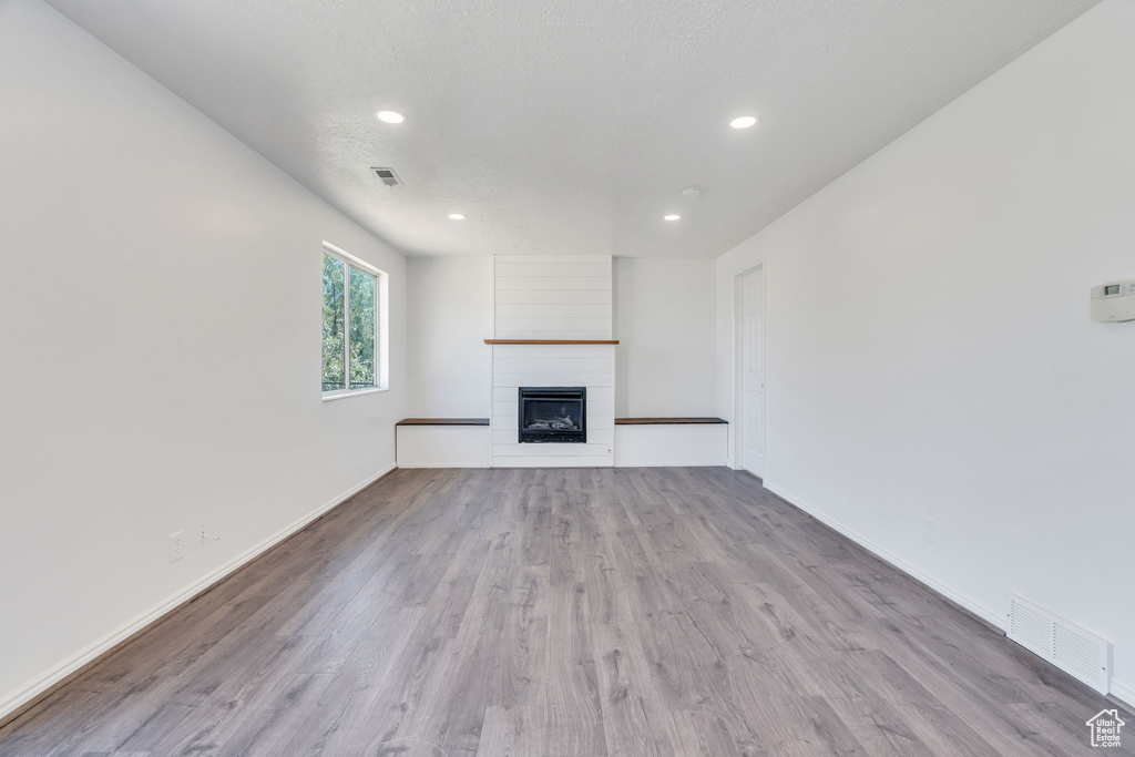 Unfurnished living room with wood finished floors, a large fireplace, and recessed lighting