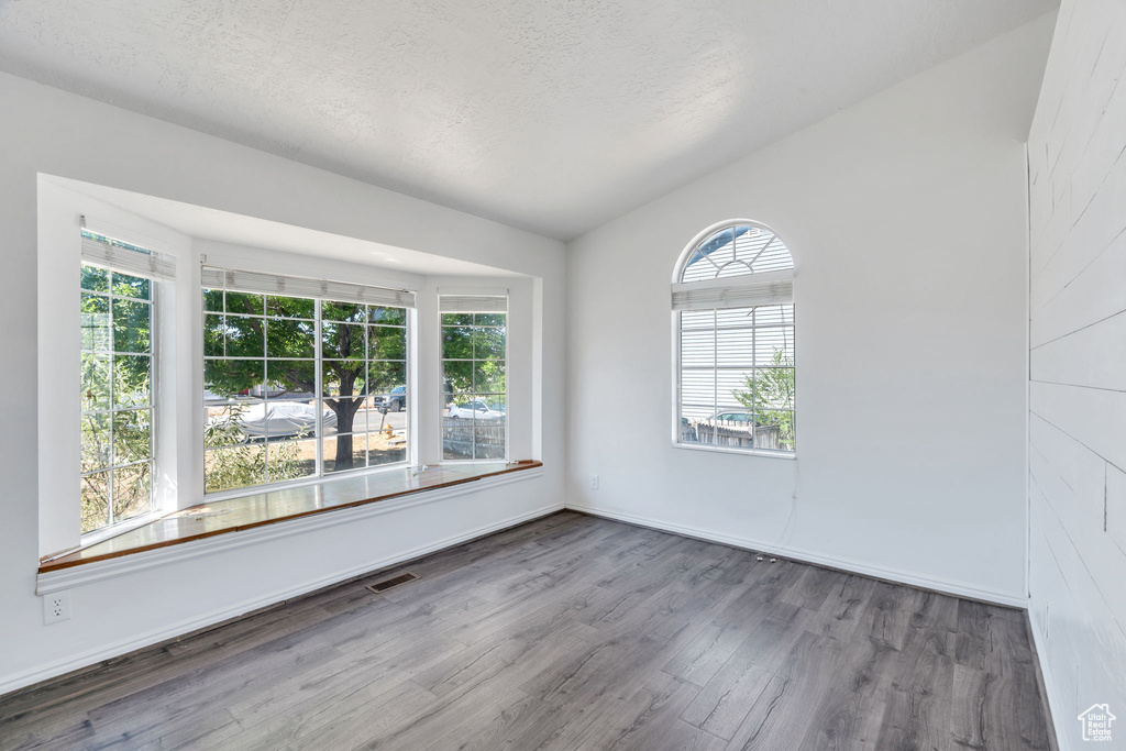 Spare room featuring wood finished floors, a textured ceiling, and vaulted ceiling