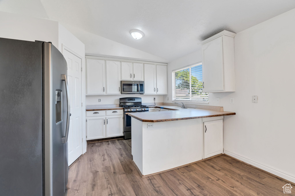 Kitchen with appliances with stainless steel finishes, a peninsula, lofted ceiling, wood finished floors, and white cabinets
