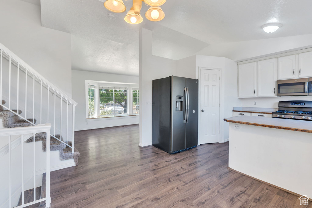 Kitchen featuring stainless steel appliances, white cabinets, lofted ceiling, dark wood-style flooring, and a chandelier