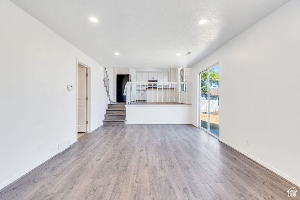 Unfurnished living room featuring light wood-style flooring, stairs, and recessed lighting