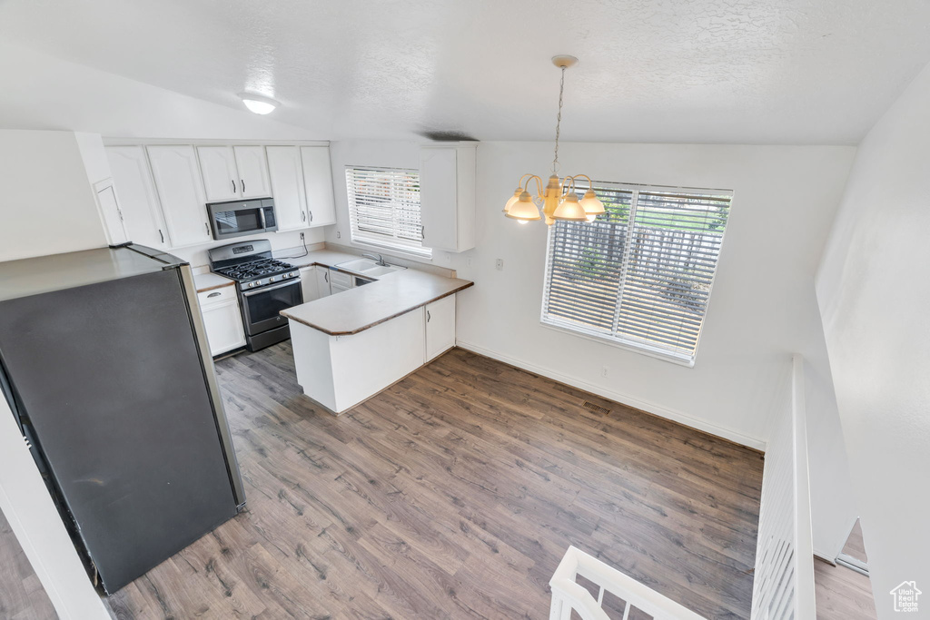 Kitchen featuring a peninsula, a chandelier, stainless steel appliances, white cabinets, and wood finished floors