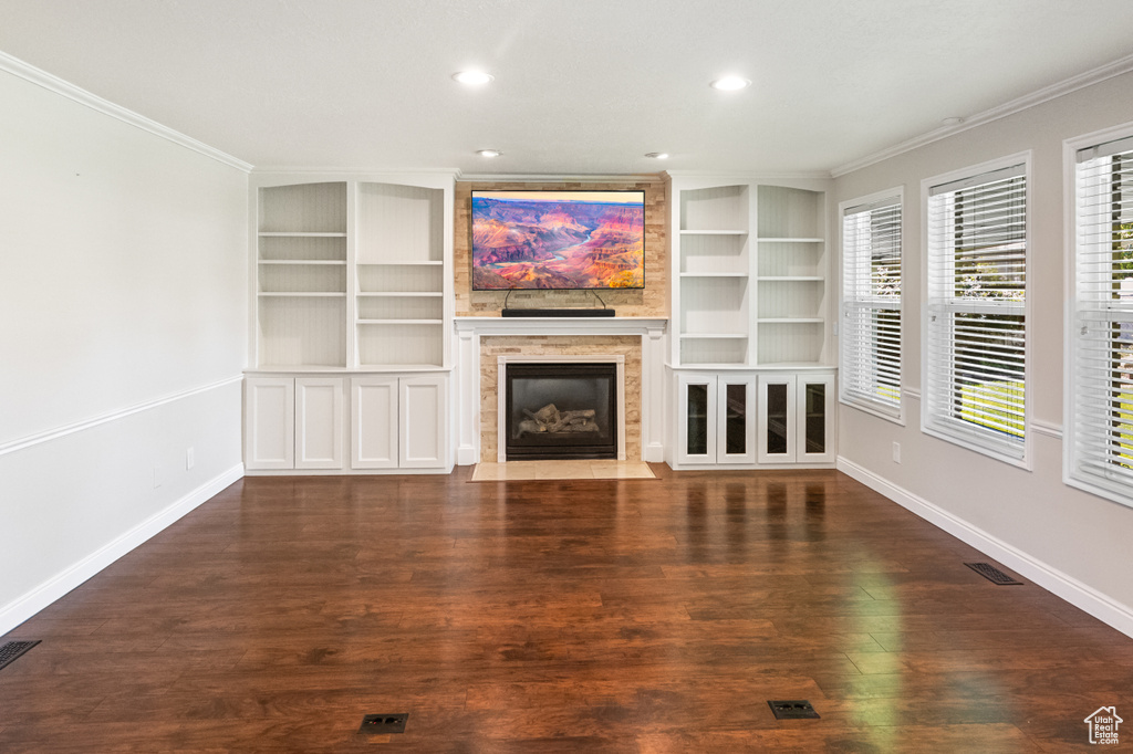 Unfurnished living room with crown molding, a fireplace with flush hearth, built in shelves, wood finished floors, and recessed lighting