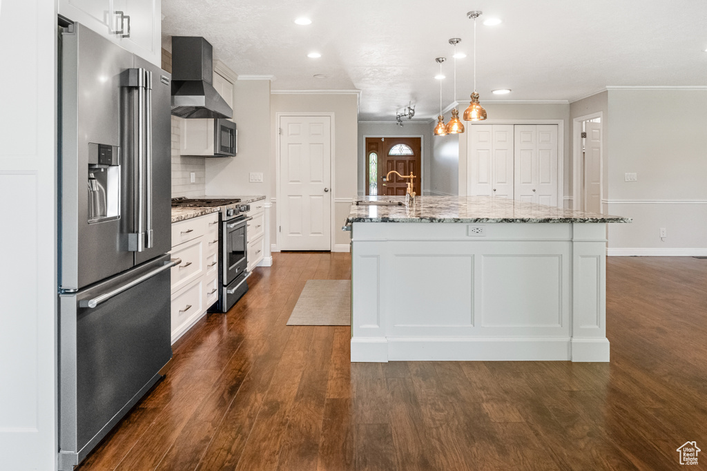 Kitchen featuring stainless steel appliances, crown molding, wall chimney range hood, a kitchen island with sink, and dark wood finished floors