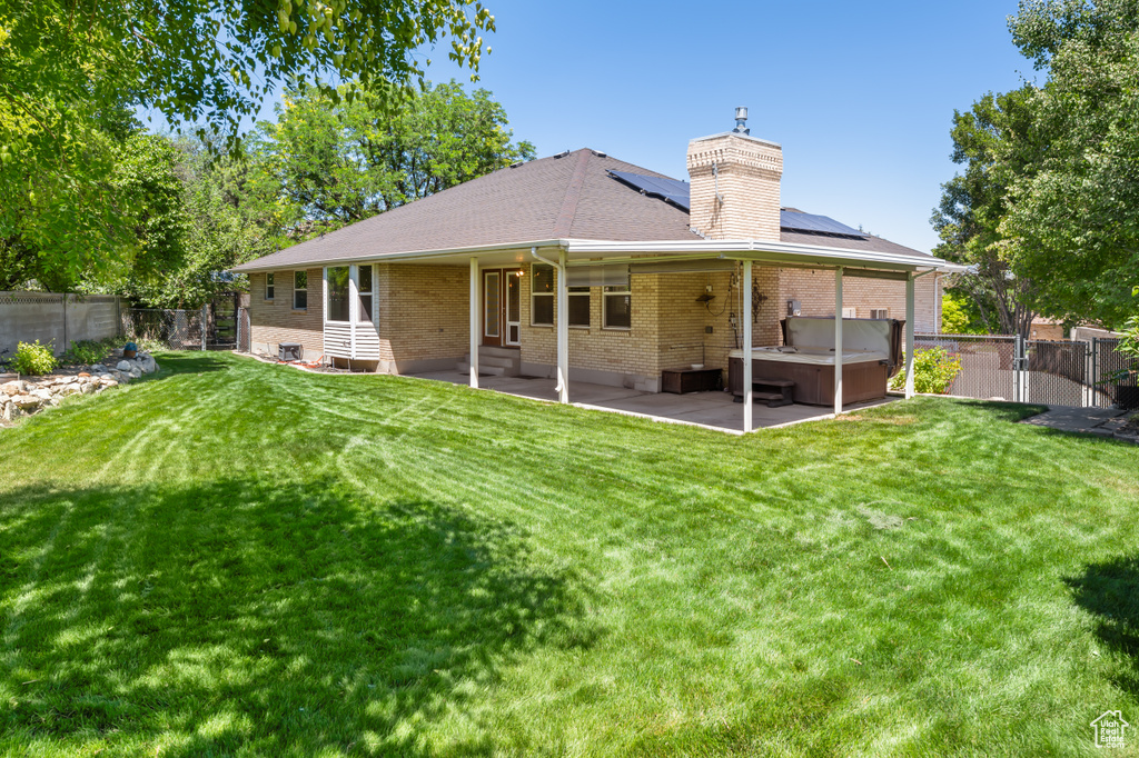 Back of property featuring a hot tub, solar panels, a patio, brick siding, and a fenced backyard