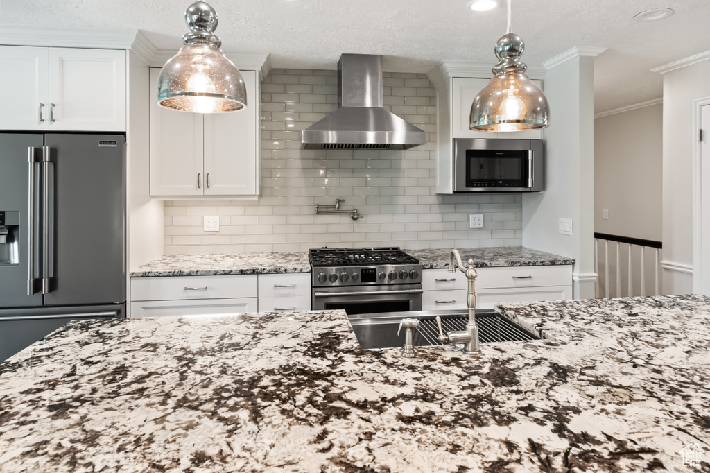 Kitchen featuring wall chimney range hood, high quality appliances, light stone counters, white cabinets, and backsplash
