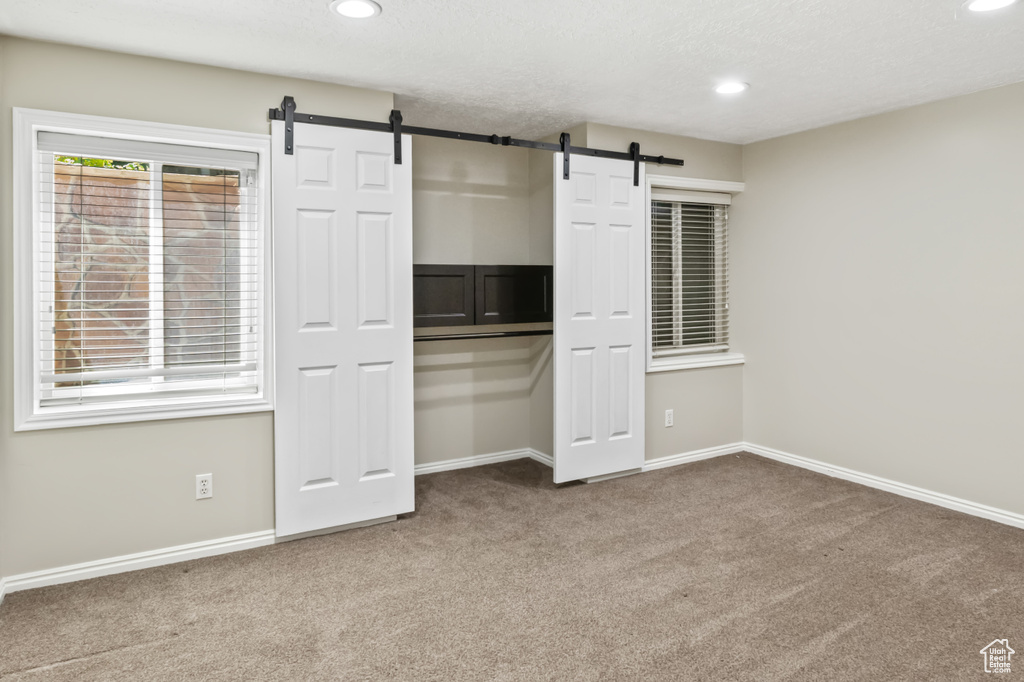 Unfurnished bedroom featuring carpet flooring, a barn door, recessed lighting, and a closet