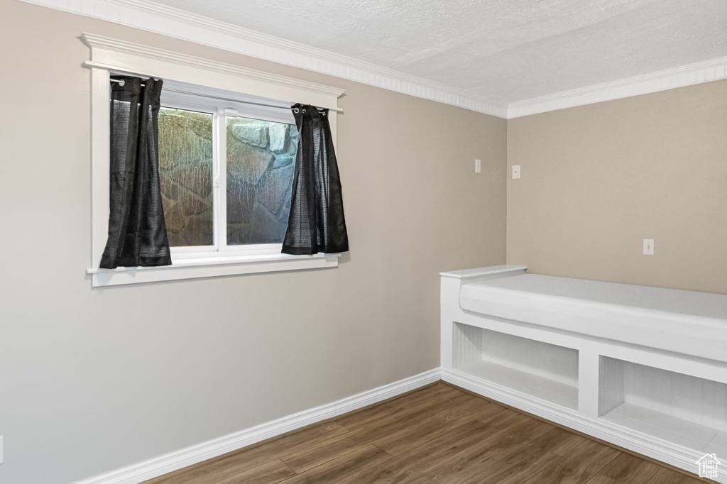 Empty room featuring wood finished floors, ornamental molding, and a textured ceiling
