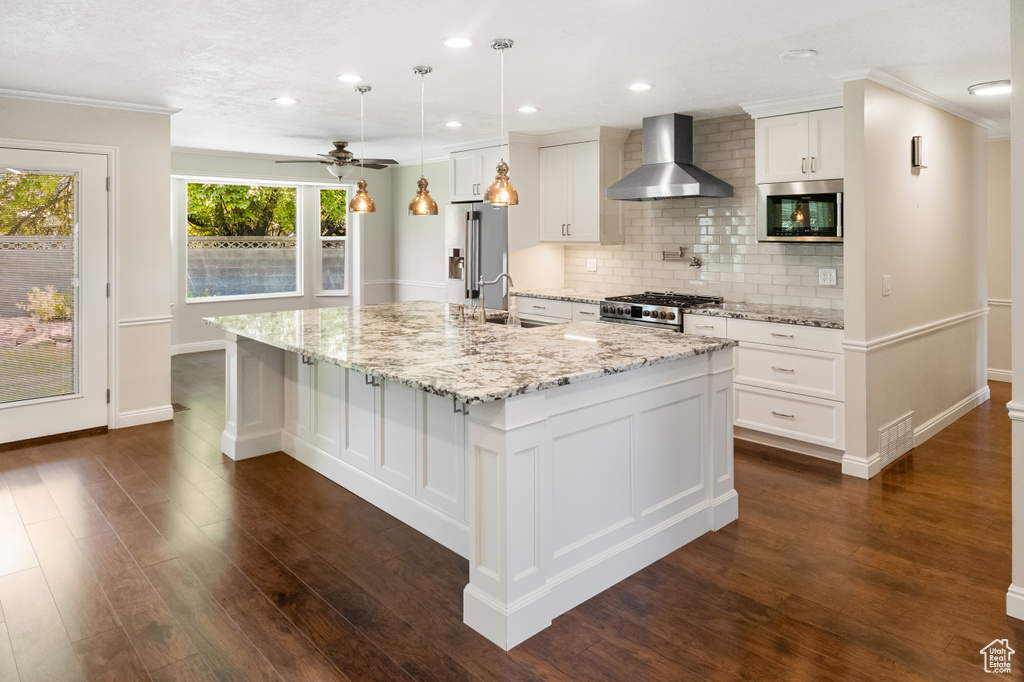 Kitchen with wall chimney range hood, backsplash, a large island with sink, dark wood-type flooring, and recessed lighting