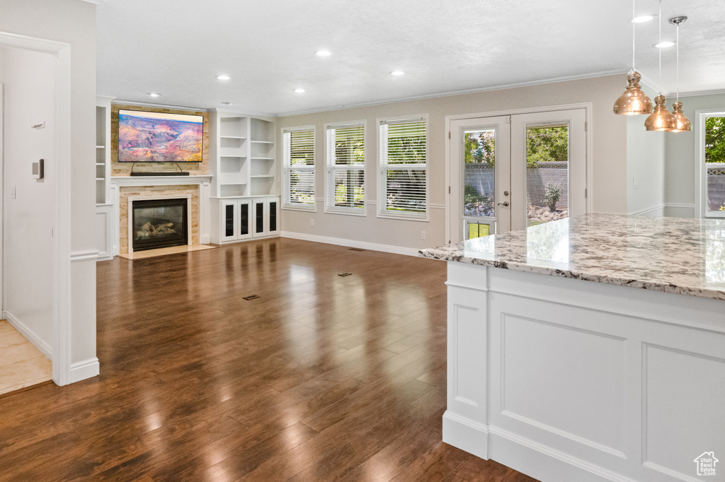 Unfurnished living room with crown molding, dark wood-type flooring, a fireplace with flush hearth, french doors, and built in features
