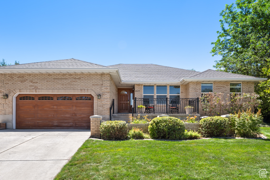 Ranch-style home with brick siding, a garage, roof with shingles, concrete driveway, and a front yard
