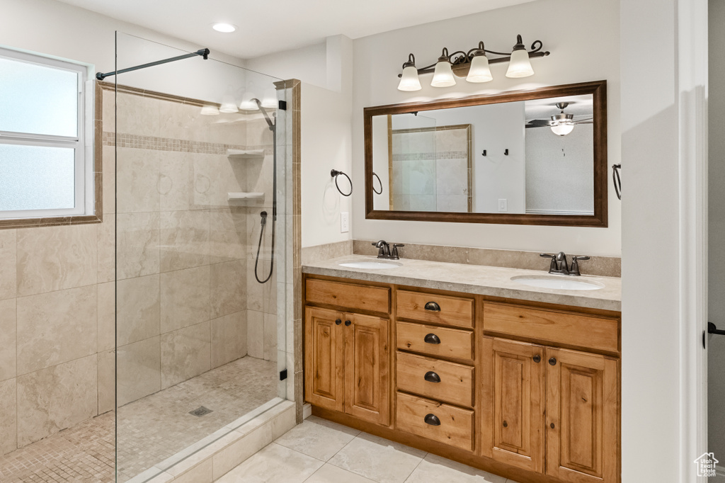 Full bath with tiled shower, double vanity, tile patterned floors, and a ceiling fan