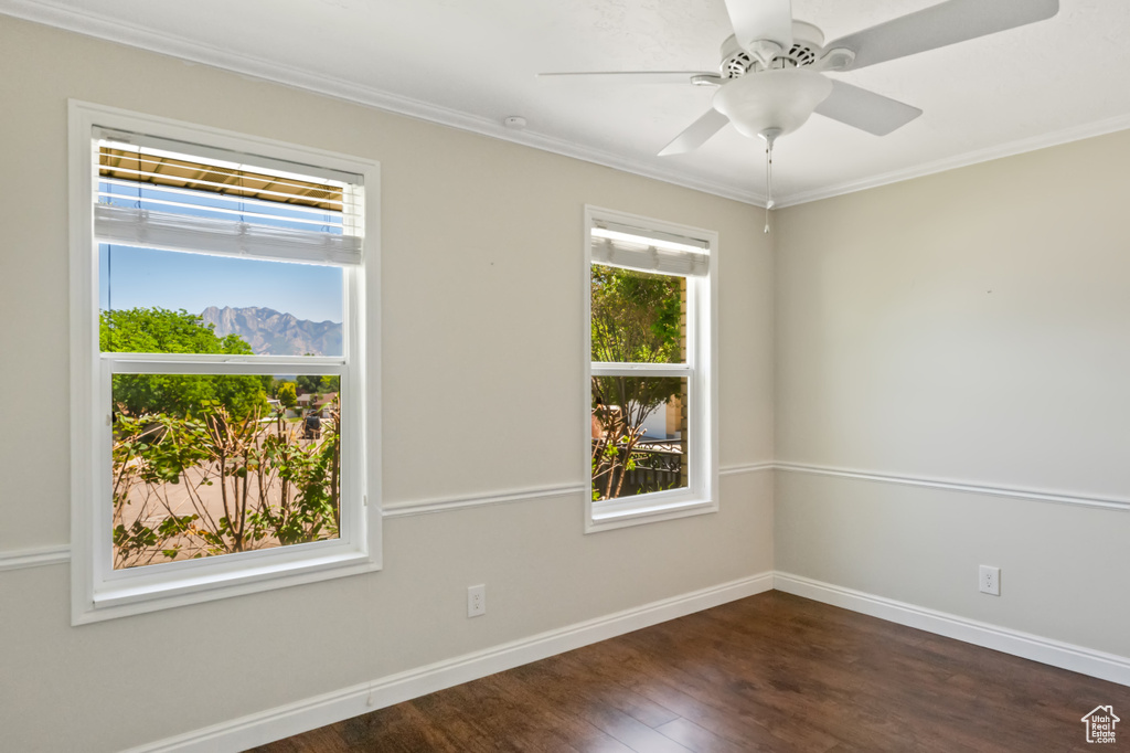 Spare room featuring dark wood-type flooring, ornamental molding, and a ceiling fan