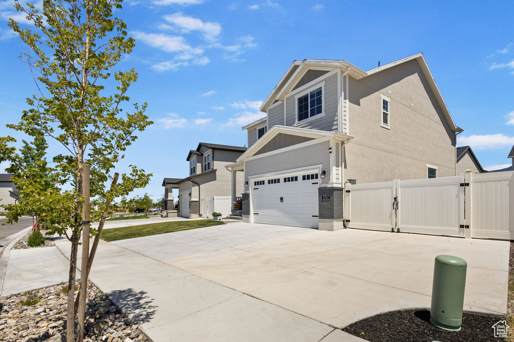 View of side of home with a gate, an attached garage, concrete driveway, and stucco siding