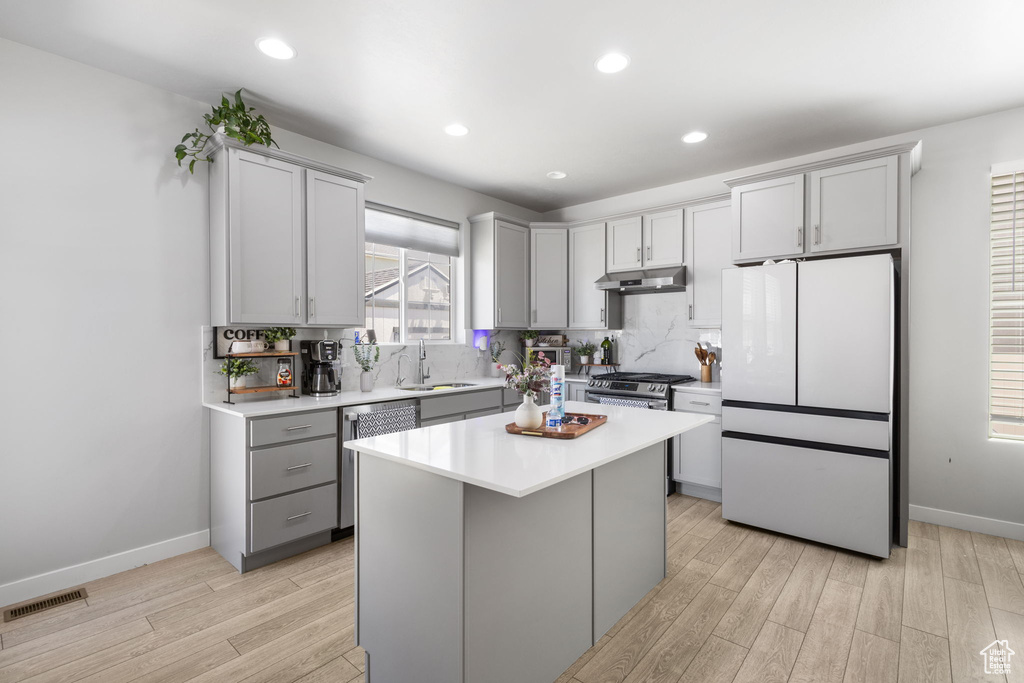 Kitchen with gray cabinetry, appliances with stainless steel finishes, light wood-type flooring, light countertops, and a kitchen island