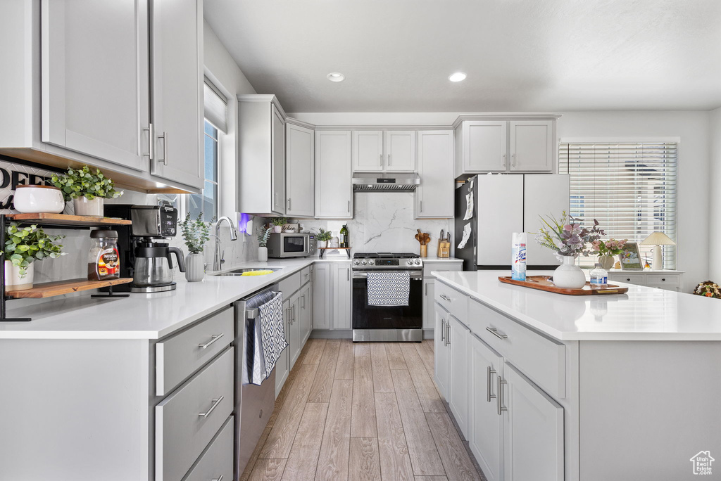 Kitchen with stainless steel appliances, light wood finished floors, light countertops, a kitchen island, and recessed lighting