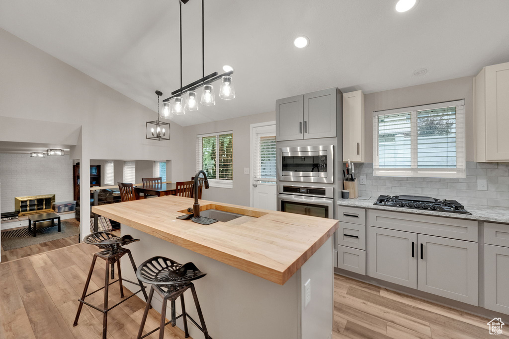 Kitchen with butcher block counters, light wood finished floors, tasteful backsplash, a breakfast bar area, and vaulted ceiling