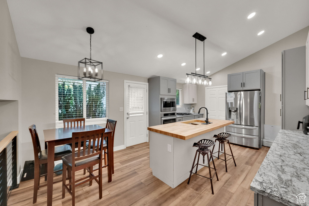 Kitchen with wooden counters, a chandelier, gray cabinetry, stainless steel appliances, and an island with sink