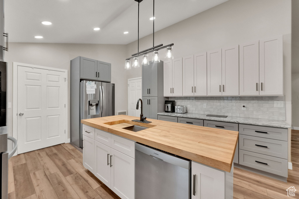 Kitchen with wood counters, appliances with stainless steel finishes, tasteful backsplash, light wood-type flooring, and a center island with sink
