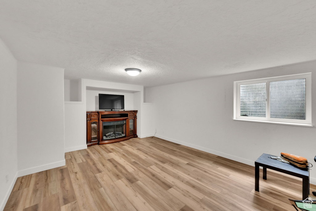Unfurnished living room with light wood-style floors, a glass covered fireplace, and a textured ceiling