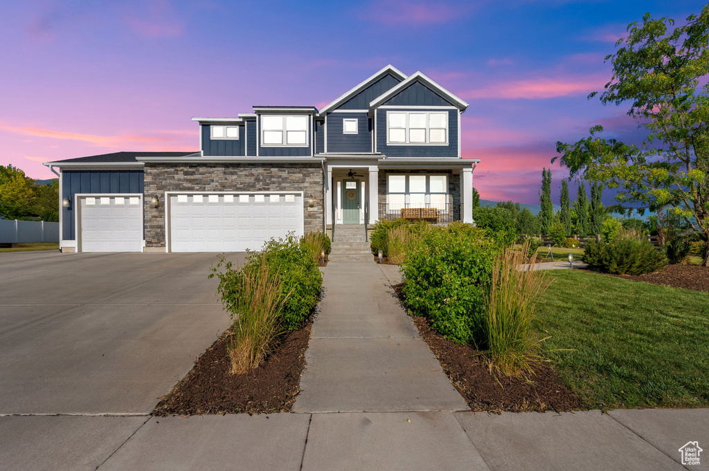 Traditional home with board and batten siding, driveway, stone siding, and a front lawn