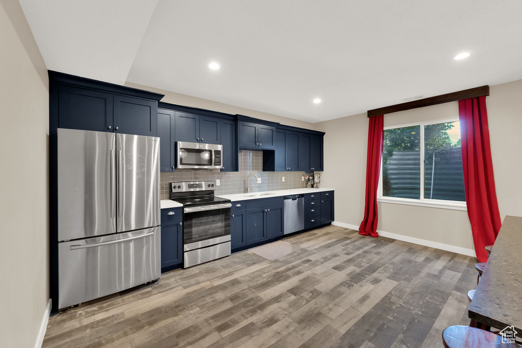 Kitchen featuring appliances with stainless steel finishes, light countertops, light wood finished floors, backsplash, and blue cabinets
