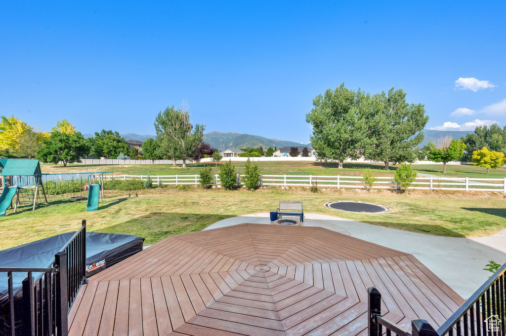 Wooden deck featuring a mountain view, a fenced backyard, and a playground