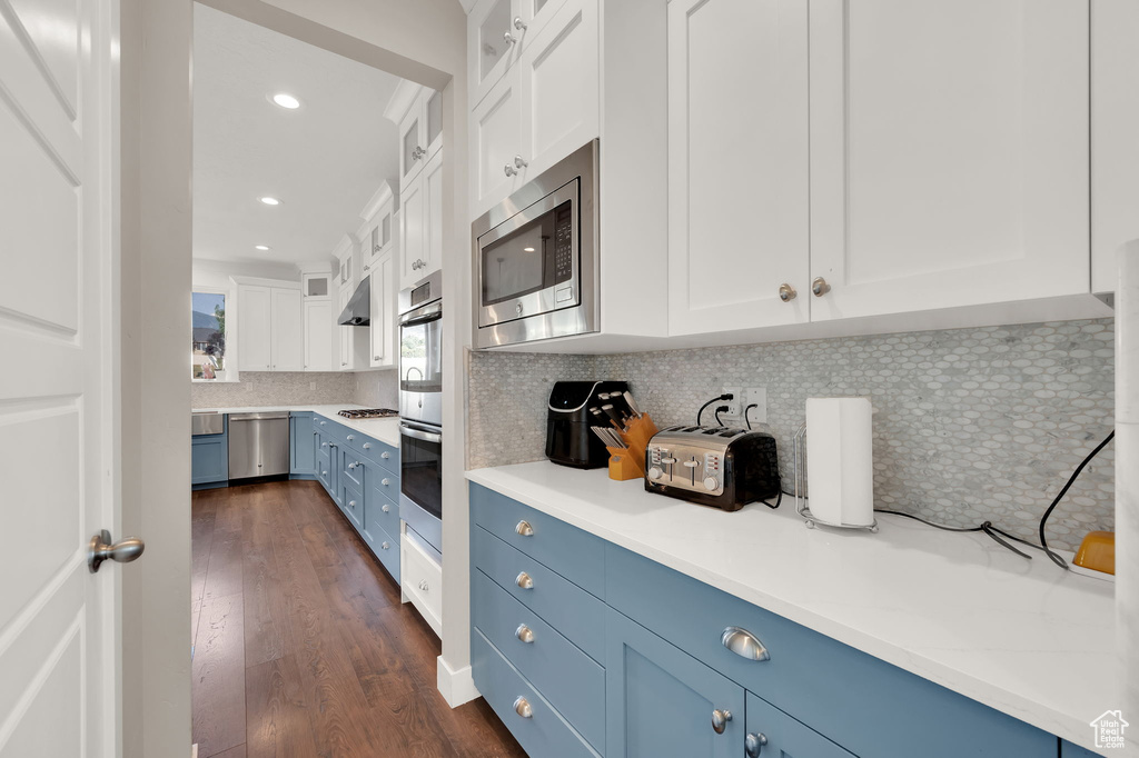 Kitchen with blue cabinets, white cabinets, dark wood-style floors, glass insert cabinets, and appliances with stainless steel finishes