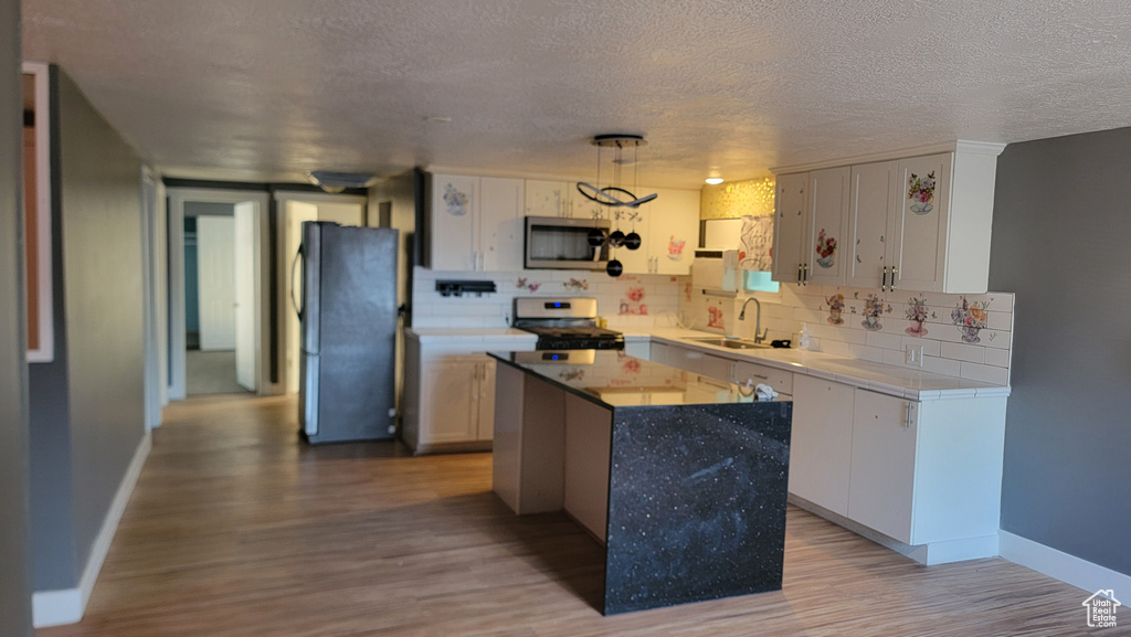 Kitchen featuring appliances with stainless steel finishes, decorative backsplash, wood finished floors, a textured ceiling, and a center island