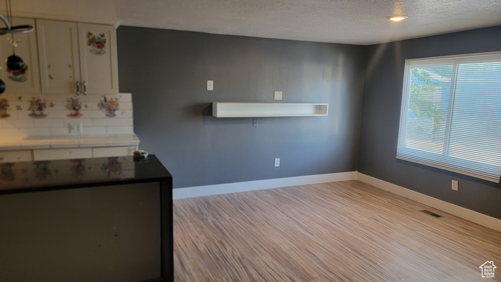 Kitchen with tile countertops, a textured ceiling, light wood-type flooring, tasteful backsplash, and white cabinets