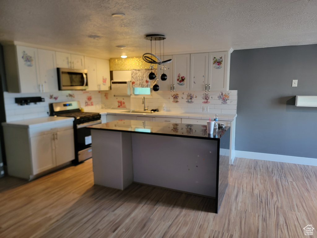 Kitchen with stainless steel appliances, white cabinets, a textured ceiling, tasteful backsplash, and light wood finished floors