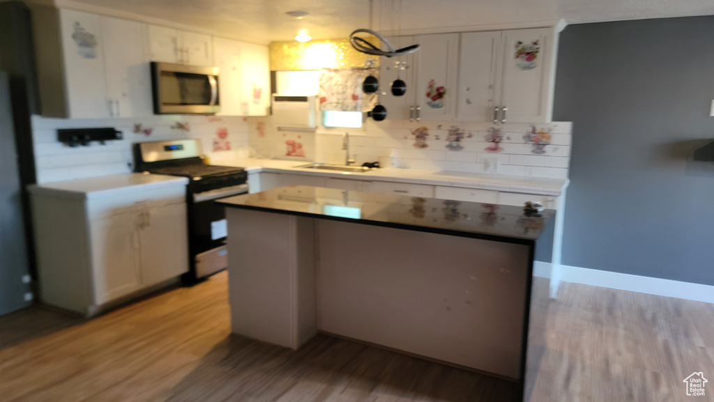 Kitchen with stainless steel appliances, tasteful backsplash, light wood finished floors, and white cabinetry