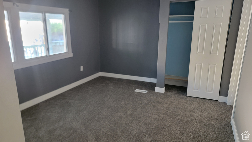 Unfurnished bedroom with dark carpet and a closet
