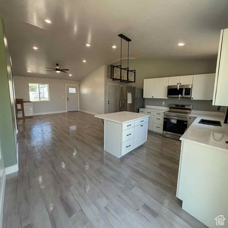 Kitchen featuring stainless steel appliances, lofted ceiling, a center island, open floor plan, and light countertops