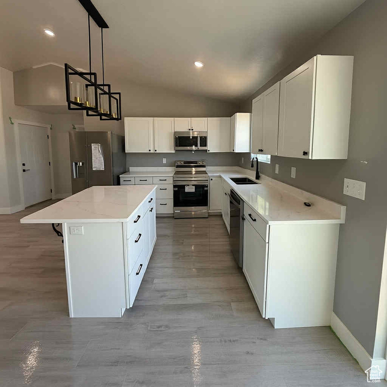 Kitchen with vaulted ceiling, appliances with stainless steel finishes, a kitchen island, white cabinetry, and recessed lighting
