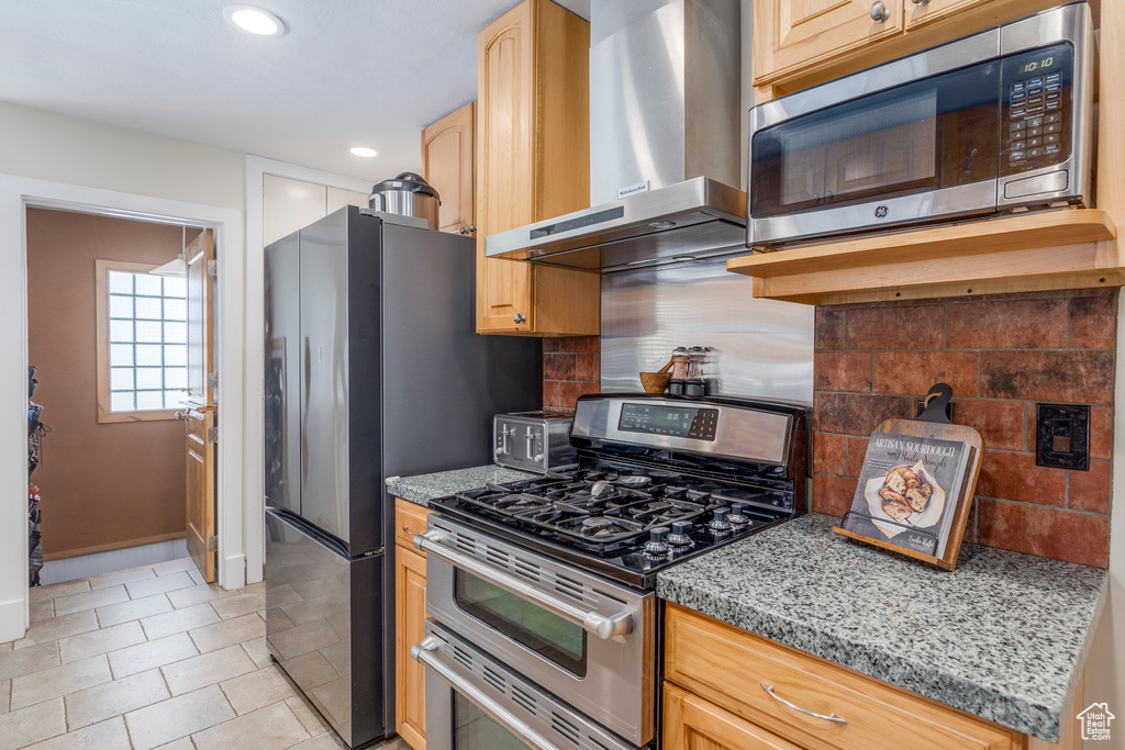 Kitchen featuring stainless steel appliances, wall chimney range hood, recessed lighting, tasteful backsplash, and light stone countertops