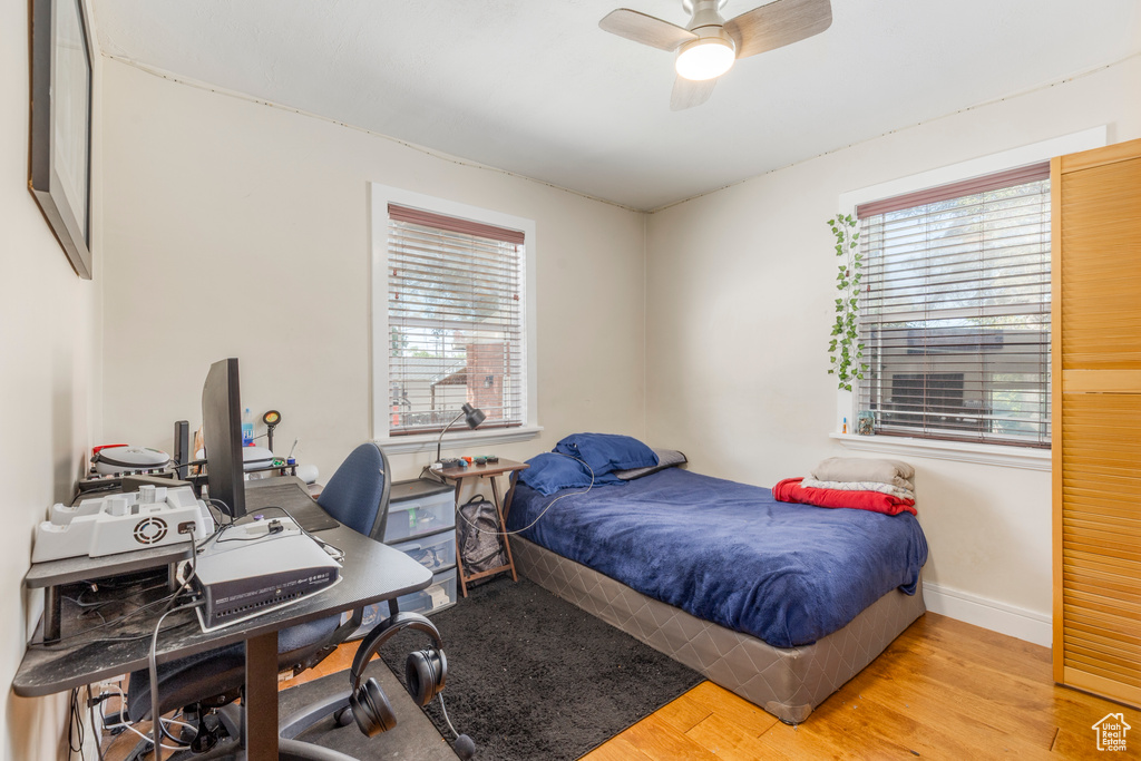 Bedroom featuring light wood finished floors, multiple windows, a desk, and ceiling fan