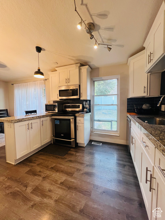 Kitchen with stainless steel appliances, a peninsula, white cabinets, track lighting, and dark wood-style flooring