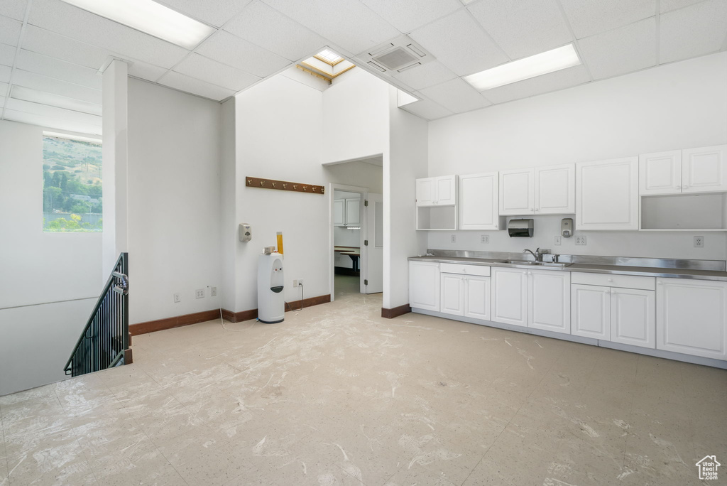 Kitchen with stainless steel counters, a drop ceiling, a towering ceiling, and white cabinets