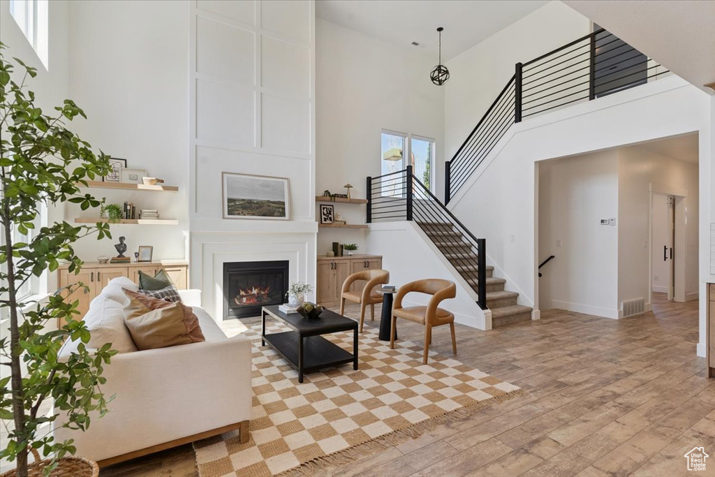 Living room featuring light wood-type flooring, a high ceiling, stairway, and a fireplace
