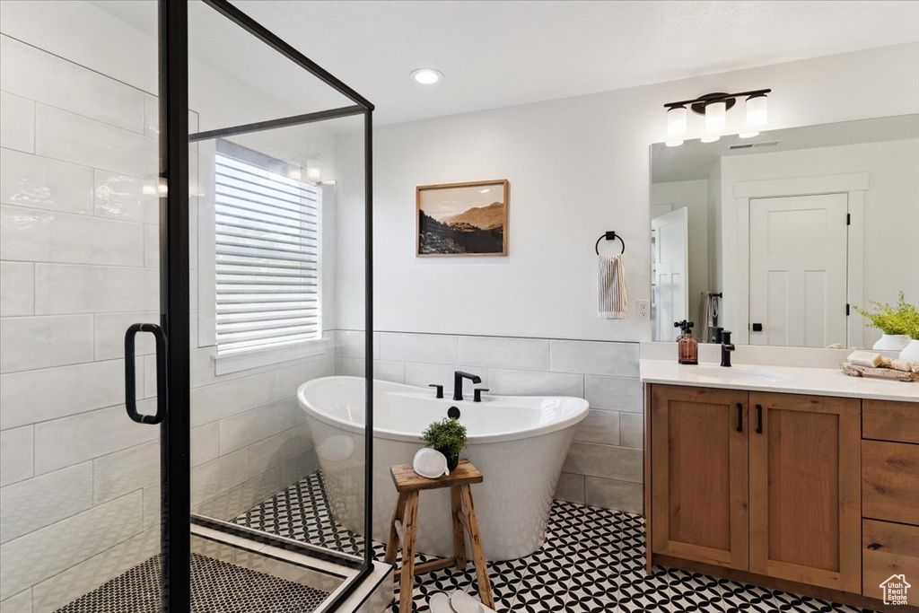 Full bathroom featuring tile walls, vanity, a stall shower, a freestanding tub, and a wainscoted wall